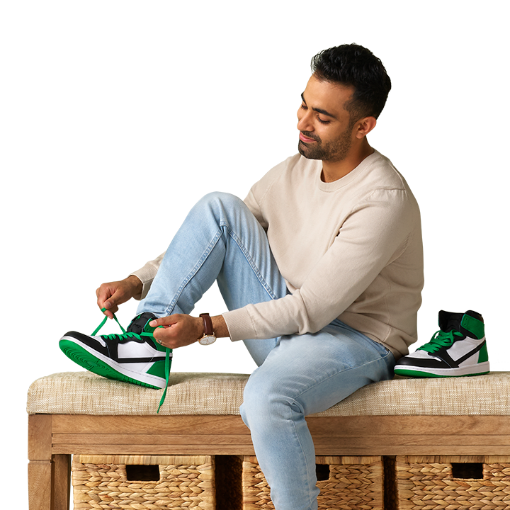 adult South Asian male sitting on a bench tying his green and white sneakers